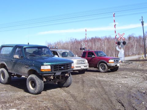 1996 Ford Bronco - Three SUVs and a pickup truck are parked near a railroad crossing on a dirt road.