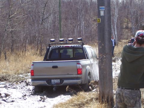 1996 Ford Bronco - A tan pickup truck navigates a muddy off-road trail, kicking up dirt as it goes.