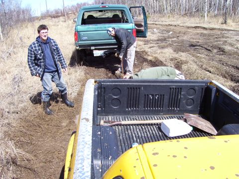 1996 Ford Bronco - Two trucks are stuck in the mud with two people attempting to free one of them.