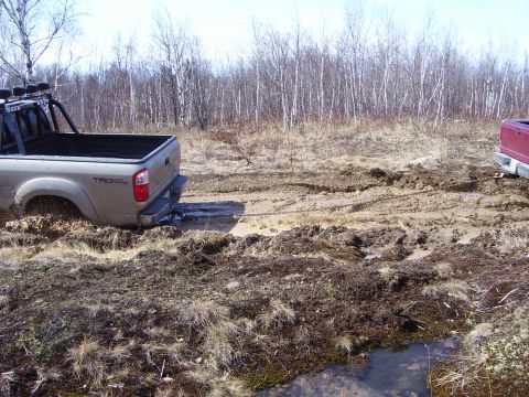 1996 Ford Bronco - A silver pickup truck is stuck in the mud, with another vehicle partially visible in the background, suggesting an off-road or recovery sit…