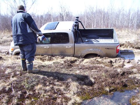 1996 Ford Bronco - Pickup truck stuck in mud with a person standing next to it.