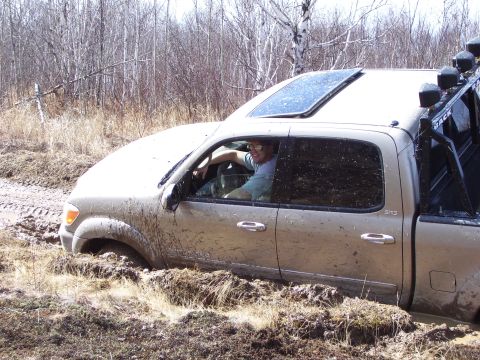 1996 Ford Bronco - A driver navigates a tan pickup truck through a muddy off-road trail, getting stuck in the mire.
