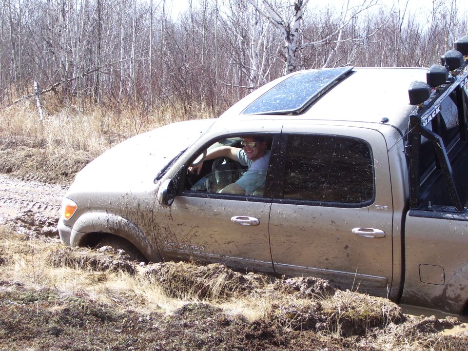 Tan pickup truck with sunroof stuck in mud, driver visible