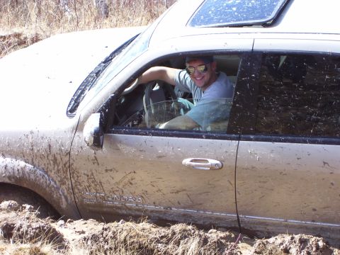 1996 Ford Bronco - Toyota Tundra stuck in mud with driver smiling.