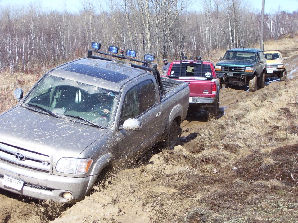 Silver Toyota Tundra stuck in mud, front view. Other trucks behind it