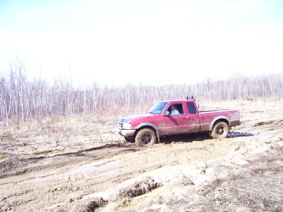Red Ford Ranger pickup truck stuck in a muddy field with trees in the background