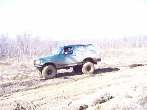 1996 Ford Bronco - A green Ford Bronco navigates a challenging muddy terrain, kicking up dirt as it goes.