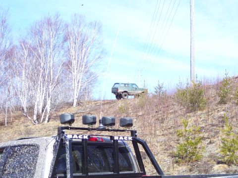 1996 Ford Bronco - A green 1996 Ford Bronco is parked on a grassy incline, with another vehicle visible in the foreground.