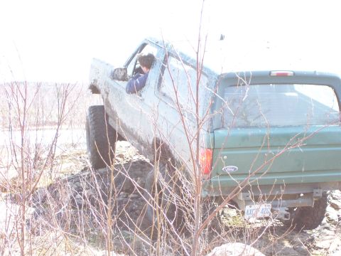 1996 Ford Bronco - A green SUV navigates a muddy, off-road terrain with its tires angled on uneven ground.