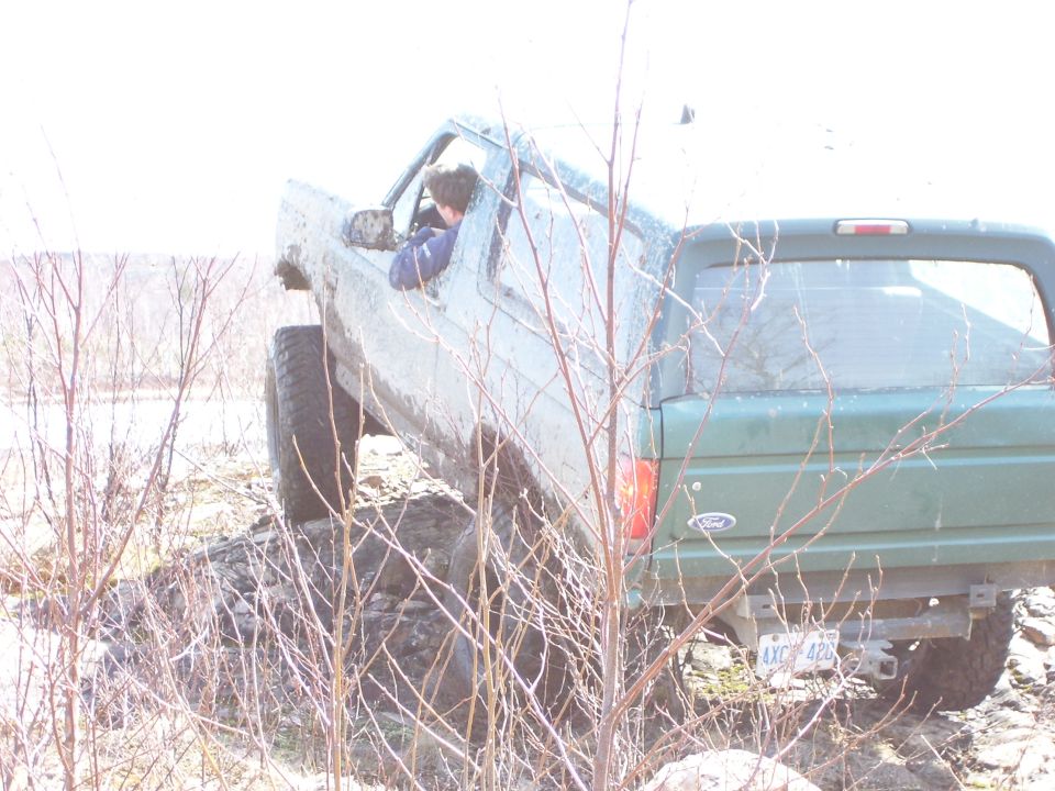 Green SUV with large tires driving off-road, driver visible through the window