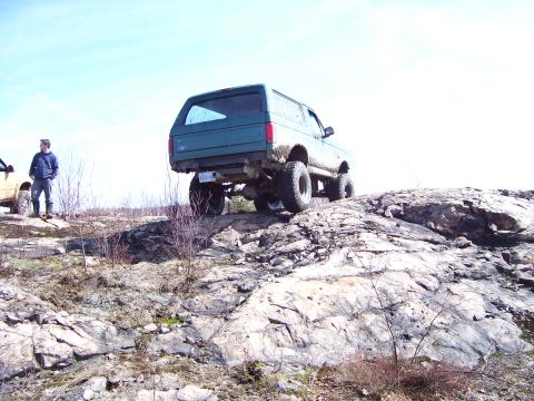 1996 Ford Bronco - A green Ford Bronco navigates a rocky incline under a clear sky.