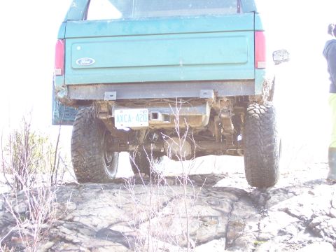 1996 Ford Bronco - The rear of a green Ford Bronco is shown, lifted with off-road tires, on a rocky terrain.