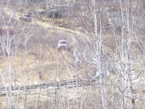 1996 Ford Bronco - Two SUVs navigate a challenging muddy terrain on a wooded hillside.