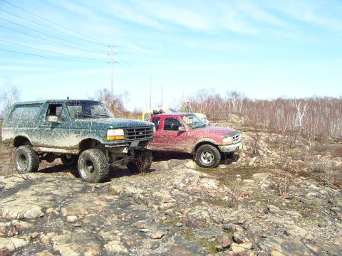 1996 Ford Bronco - Two 4x4 vehicles, a green Bronco and a red pickup, navigate a rough, rocky landscape under a clear sky.