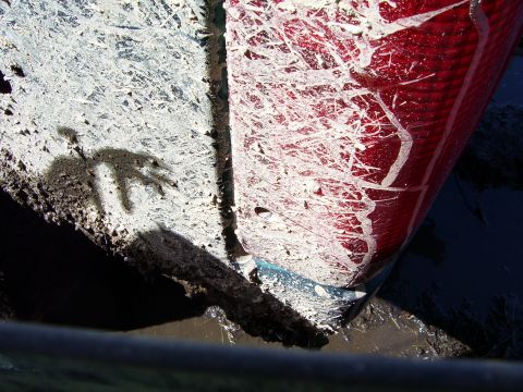 1996 Ford Bronco - Close-up of a muddy vehicle's rear corner, showing a red taillight and white body panel covered in white paint splatters.