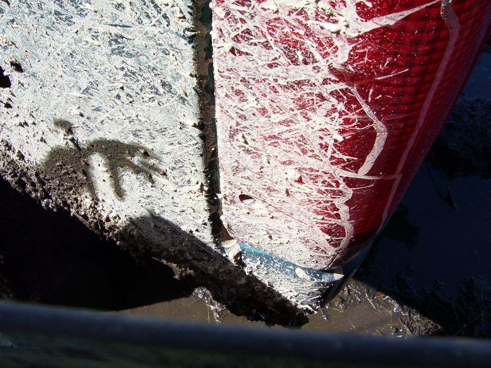 Mud splattered on a red taillight and white body panel. Shadow of a hand is visible on the white panel