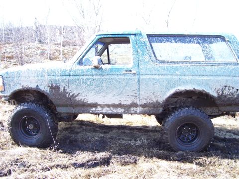 1996 Ford Bronco - A heavily muddied 1992 Ford Bronco is shown from the side, navigating a wet, grassy area.