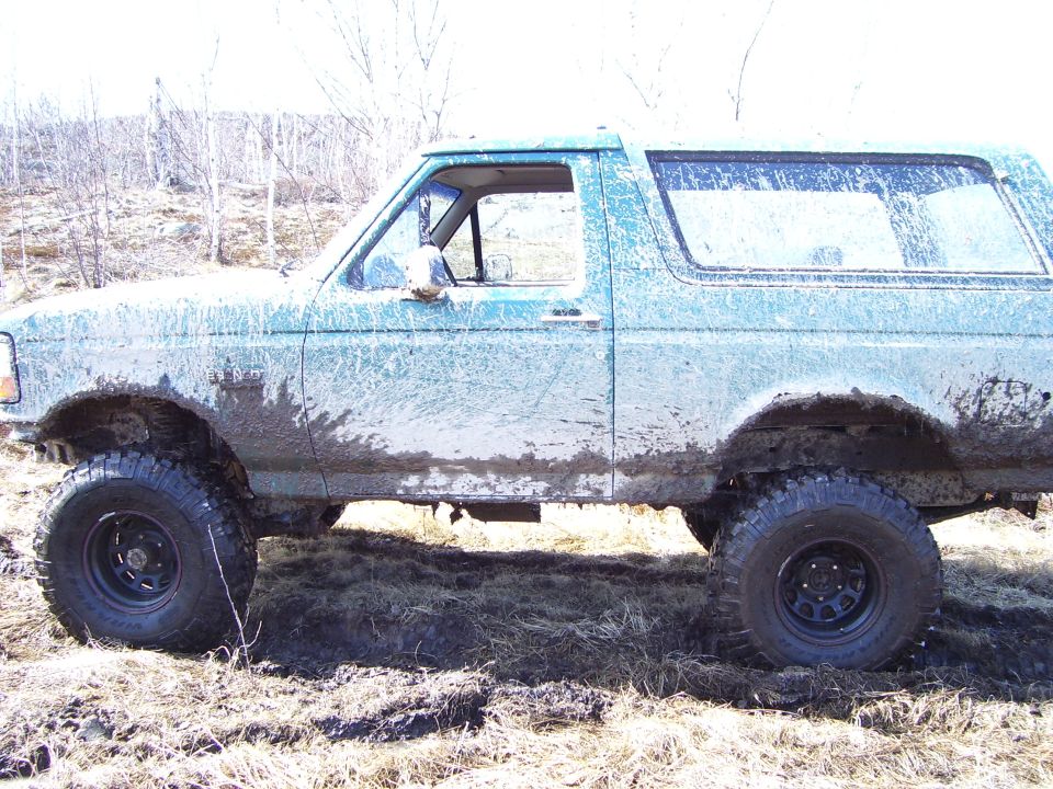 Mud-covered teal 1992 Ford Bronco, side view, with off-road tires on uneven terrain