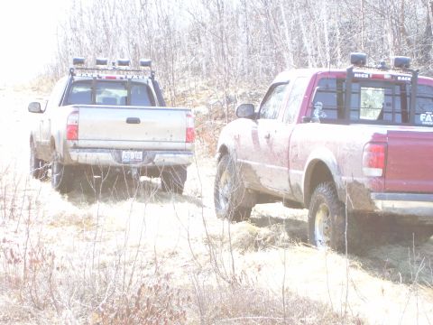 1996 Ford Bronco - Two pickup trucks navigate a dirt path surrounded by dry brush and trees.