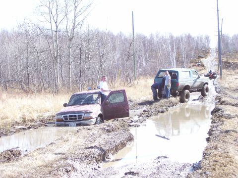 1996 Ford Bronco - Two trucks are stuck in the mud on an off-road trail, with people attempting to free them.