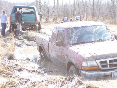 1996 Ford Bronco - Two vehicles, a red Ford Ranger and a green Ford Bronco, are stuck in the mud off-road.