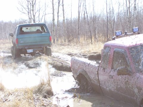1996 Ford Bronco - A green 1996 Ford Bronco is being pulled from a muddy ditch by a red pickup truck.