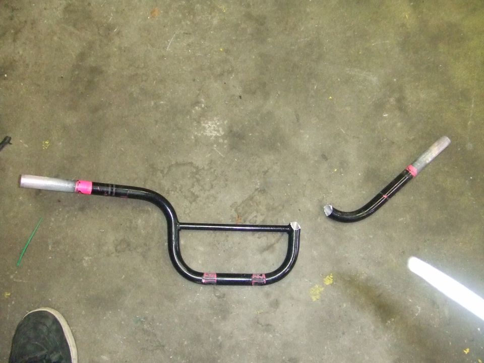 Black motorcycle handlebars, one piece broken, lying on a concrete floor
