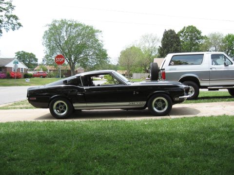 1968 Shelby GT500 - A black 1968 Shelby GT500 is parked next to a silver SUV, showing its distinctive side profile and GT500 badging.
