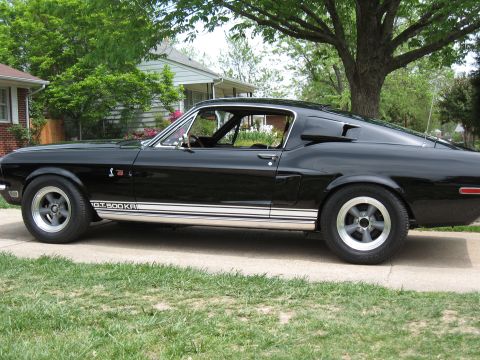 1968 Shelby GT500 - This black 1968 Shelby GT500KR coupe is seen from the side, parked in front of a residential house.