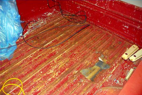 1979 Ford F-150 - The bed of a truck shows significant rust and damage to its red paint finish.
