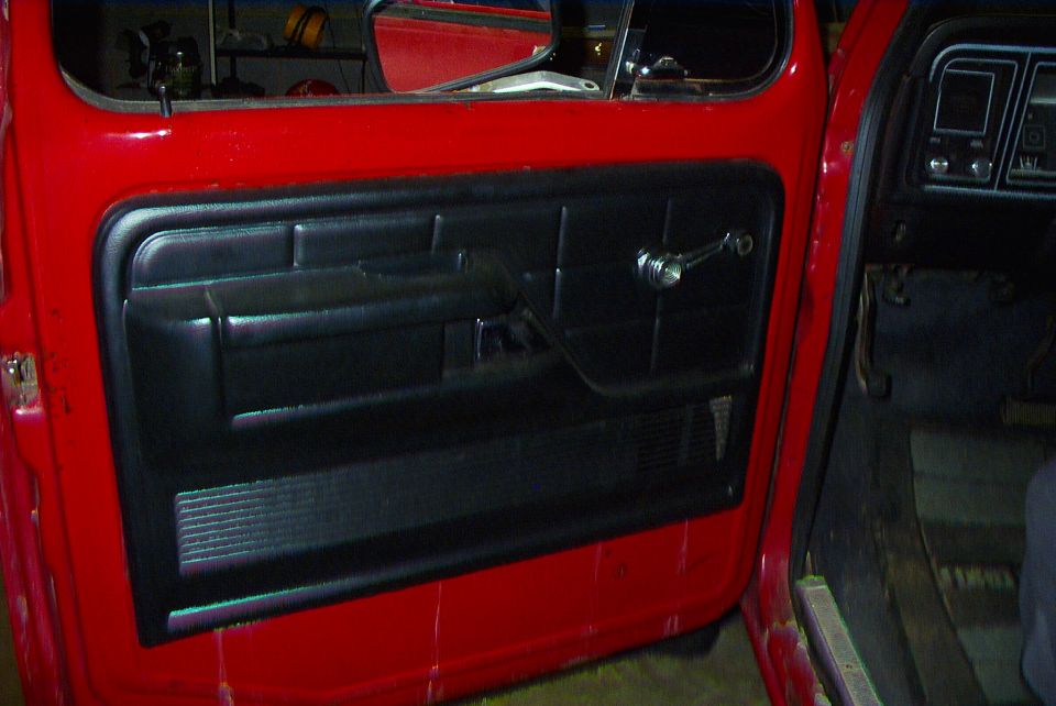Black vinyl door panel with chrome window crank inside a red pickup door