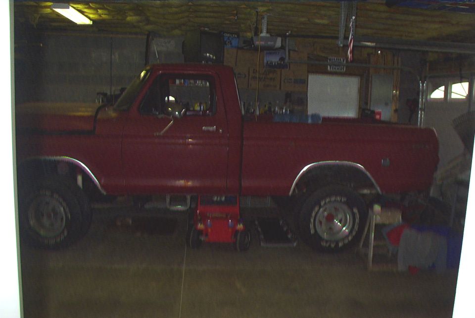 Driver side profile of a lifted red Ford regular cab pickup in a garage