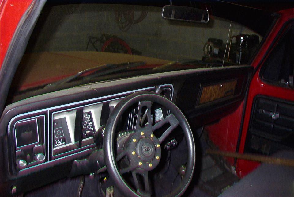Truck interior with black aftermarket steering wheel and dashboard, viewed toward windshield.