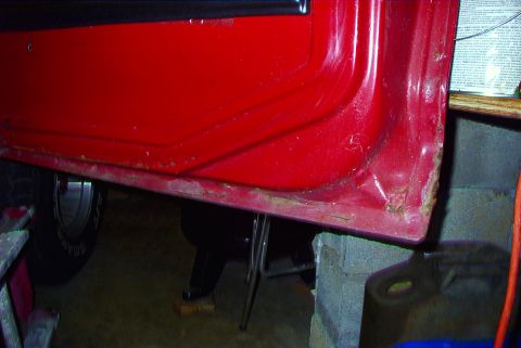 1979 Ford F-150 - Close-up view of a red vehicle's door sill, revealing significant rust and damage.