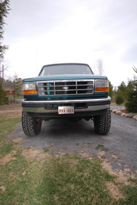 1996 Ford Bronco - This teal Ford F-150 pickup truck is shown from the front, a chrome grille and large off-road tires.