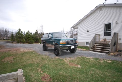 1996 Ford Bronco - A green Ford Bronco is parked on a gravel driveway beside a white house with a dog on the steps.