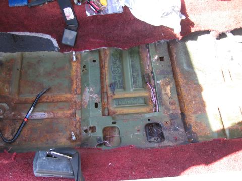 1973 Ford Ranchero - Interior view of a vehicle's floor pan showing significant rust and a seatbelt buckle.