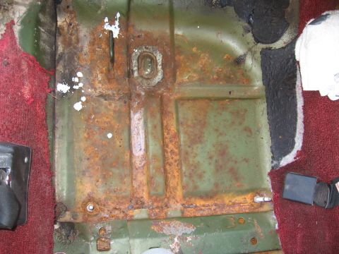 1973 Ford Ranchero - The interior floor pan of a vehicle shows significant rust and wear, with remnants of carpet and a seatbelt visible.