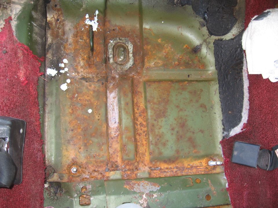 rusted green floor pan with red carpet and seatbelt buckle