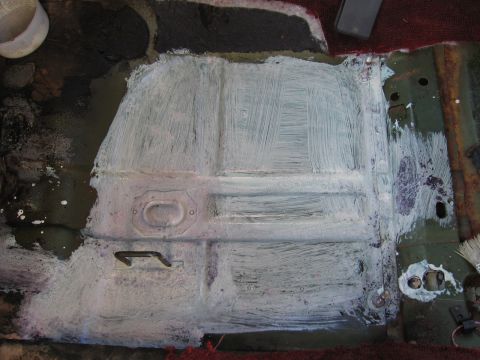 1973 Ford Ranchero - The floor pan of a vehicle is covered in white primer, revealing its ribbed metal structure and a small handle.