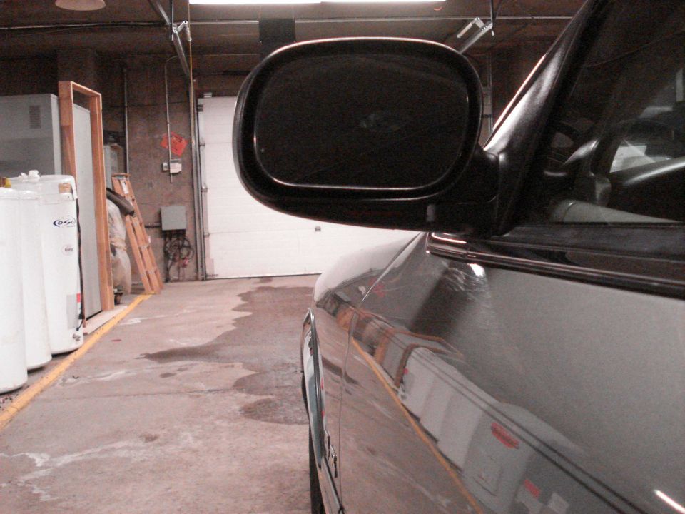 Black side mirror and fender of dark gray sedan parked in a garage with white garage door behind