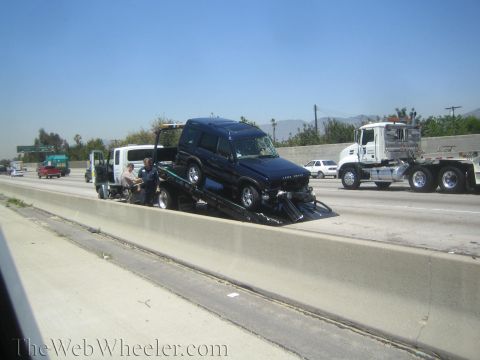 1987 Suzuki Samurai - A dark blue Land Rover Discovery is loaded onto a tow truck on a sunny day on the highway.