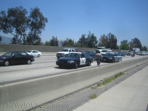 1987 Suzuki Samurai - Multiple police vehicles and other traffic are stopped on a highway, with a law enforcement officer walking between two patrol cars.
