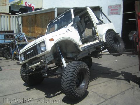 1987 Suzuki Samurai - A modified Suzuki Samurai is shown on a lift, highlighting its custom suspension and large off-road tires.