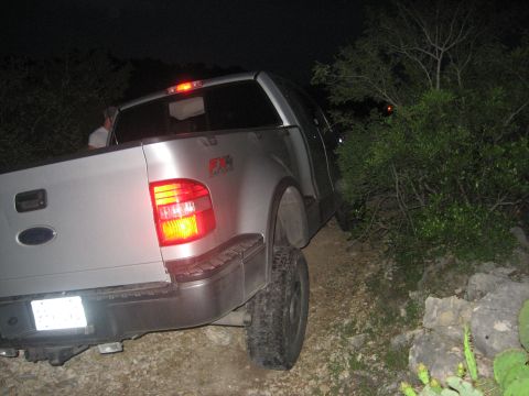 1979 Ford Bronco - A silver pickup truck is partially obscured by brush on a dirt path at night.