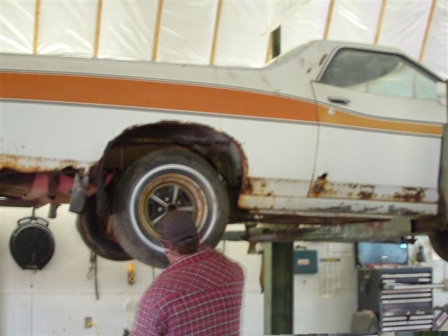 1975 Ford Ranchero on a lift, showing rust around the rear wheel well and lower body panels