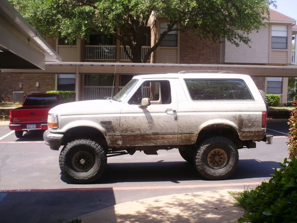 White Ford Bronco parked next to a red pickup truck. It's covered in mud