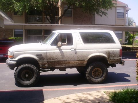 1992 Ford Bronco - A muddy white 1992 Ford Bronco is parked outside an apartment building.