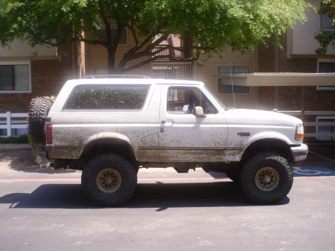1992 Ford Bronco - A muddy white 1992 Ford Bronco is shown from the side, parked in front of a building.