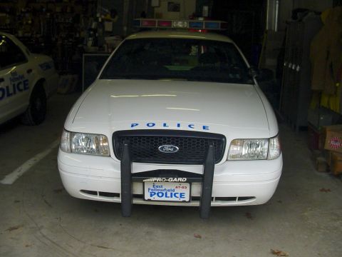 2002 Ford Crown Victoria - A white police car is parked inside a garage, with another police car partially visible to its left.